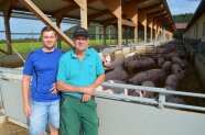 Zwei Männer stehen vor einem Freiluftschweinestall mit Heustreu