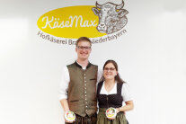 Mann und Frau stehen vor einem Schild mit dem Betriebsnamen